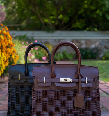 Two handbags, one black and one brown, on a stone surface with a garden background.